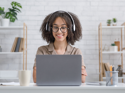 Woman wearing headphones and smiling at an open laptop screen.