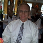 Stephen Bauer head and shoulders photograph. Photo of a man with glasses wearing a white shirt and tie.