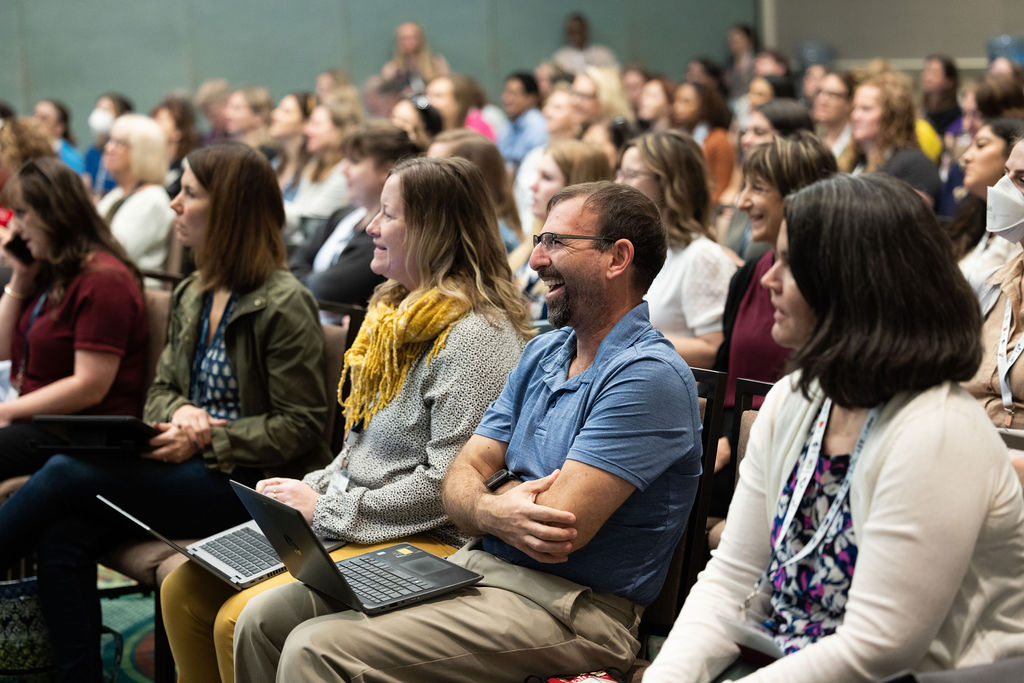 Lively audience sits in chairs at ATIA 2023 and laughs at what the speaker says.
