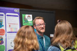 A gentleman and two ladies at ATIA 2024 network and chat around the poster session area.