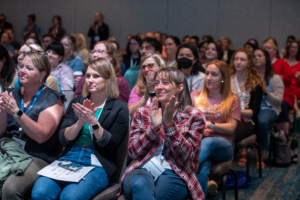 Past attendees at the ATIA conference are smiling and clapping after listening to an education session.