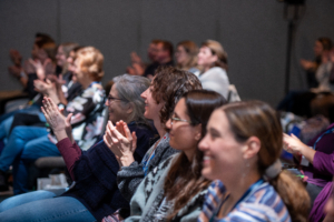 ATIA 2024 attendees clap and smile as 2024 Prentke Lecture recipient, Karanveer Singh, gives his lecture.