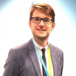 Picture of Charlie Danger wearing a gray sports coat over a  white button up shirt with a black tie.
