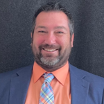Picture of Chris Smith wearing a salmon colored shirt with a tie over a blue sports coat.
