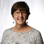 Picture of Wendy Rogers wearing blue earrings and a silver necklace with a brown and white paisley blouse.
