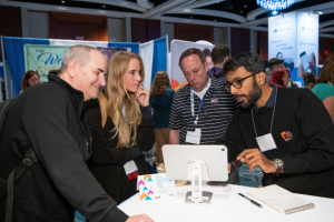 Attendees watching an exhibitor demonstrate an assistive technology product on a tablet at the ATIA conference.